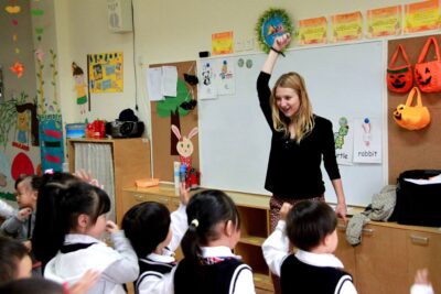 English teacher in Suzhou China, raising her hand in front of the whiteboard 